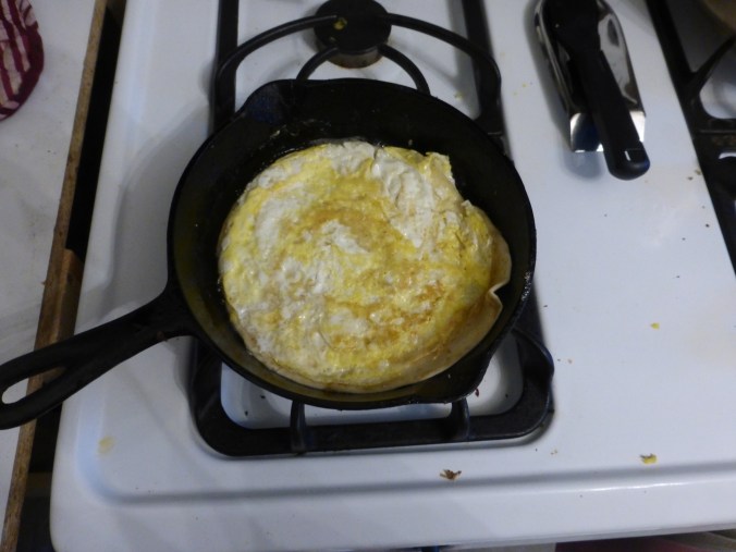 flat circle of cooked egg in pan with tortilla sticking up at the edge