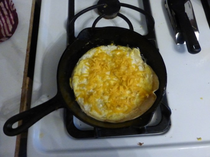 grated cheese sprinkled over egg on tortilla in pan