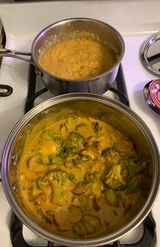 two pots on stove: vegetables in yellow curry sauce in front, red lentils in back