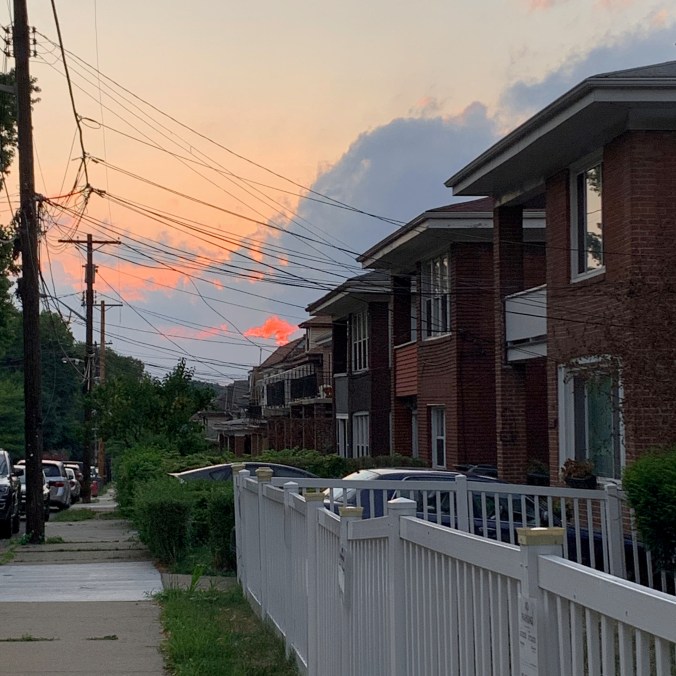 sunset seen through power lines above a row of brick duplexes and sidewalk