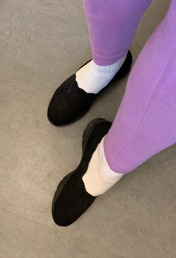 feet in black slip-on shoes made of a lacy fabric, with grippy rubber soles