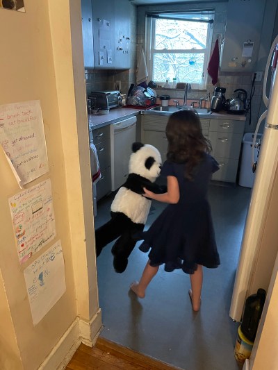 a little girl dancing with a large stuffed panda, in her kitchen; snowy branches visible out the window