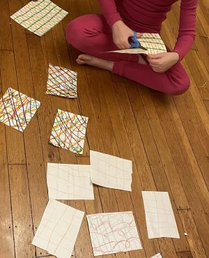 child cutting up paper on which complex plaid patterns have been drawn with markers
